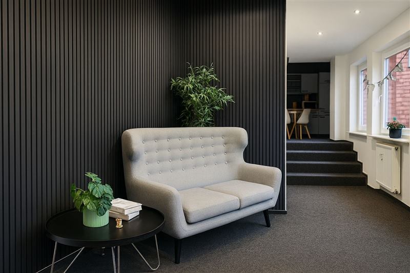 Lounge mit grauem Sofa vor dunkler Lamellenwand